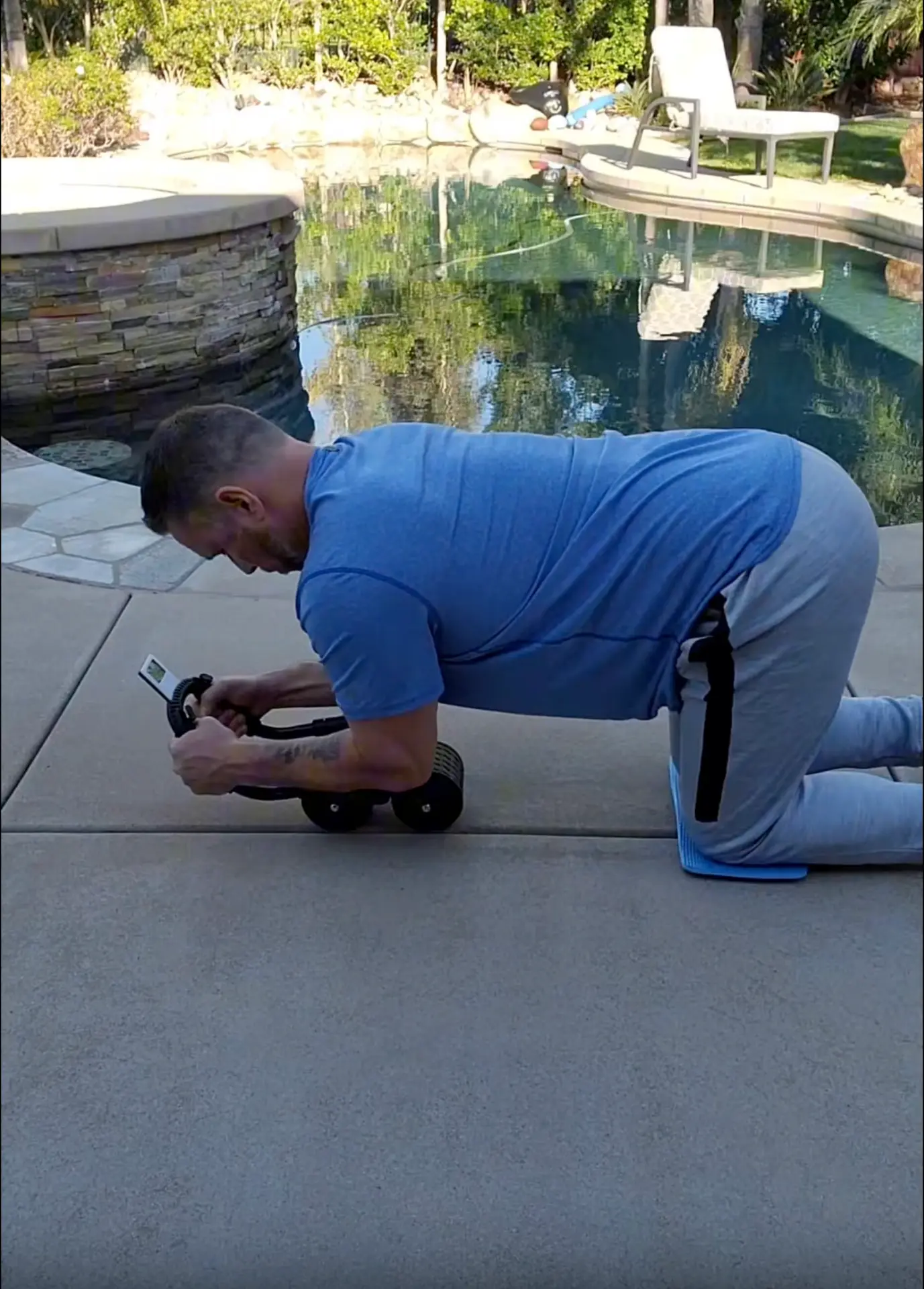A man using the PostureFlex Ab Roller outdoors on a pool deck