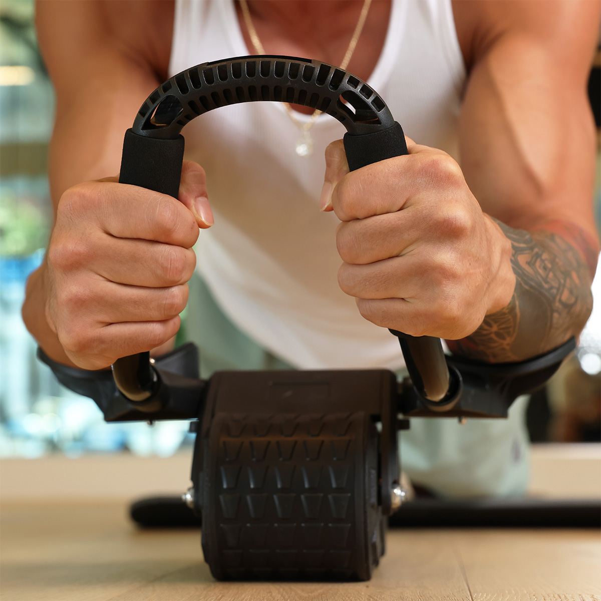 Close-up of hands gripping the PostureFlex Ab Roller handles with padded forearm support and two wide wheels